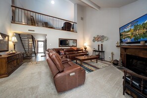 Ein geräumiges Wohnzimmer mit einem braunen Ledersofa, einem Flachbildfernseher, einem Kamin und einer Treppe, die in einen oberen Bereich führt.