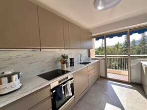 A modern kitchen with a built-in oven, a sink, and a window overlooking a balcony. - Marina view apartment, terrace & pool (Mandelieu-la-Napoule)