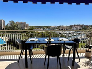 A balcony with a table set for two, overlooking a marina with boats. - Marina view apartment, terrace & pool (Mandelieu-la-Napoule)
