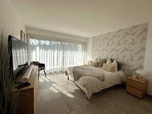A bedroom with a bed, bedside tables, a TV, and a window with sheer curtains. - Marina view apartment, terrace & pool (Mandelieu-la-Napoule)