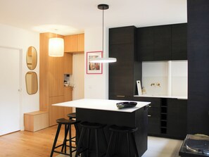 Eine moderne Küche mit einer zentralen Kochinsel, Barhocker, Holzschränken und Pendelleuchten.