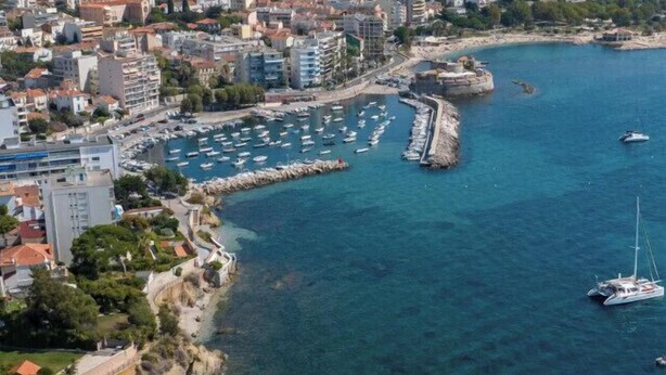 Vue aérienne d’une ville côtière avec un port de plaisance, des bâtiments et une côte rocheuse.