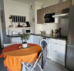 A compact kitchen with a washing machine, microwave, and a small dining area with a table and chairs. - Apartment with terrace and garden in Audenge (Audenge)