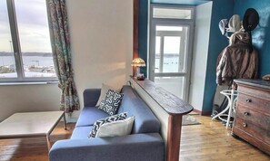 A room with a sofa, a small table, a dresser, a lamp, a view of the sea, and a door. - House by the sea Avel Vor (Ploubazlanec)