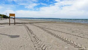 En strand med fodaftryk, der fører til vandet, et fareskilt og en klar himmel.
