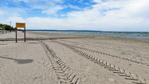 A beach with footprints leading to the water, a caution sign, and a clear sky. - Wasaga Beach Riverfront, Walk to Beach 1, Sleeps 10, Pet-Friendly, 95 Mosley St (Wasaga Beach)