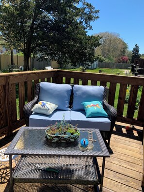 Une terrasse en bois avec un canapé en osier et une table à plateau en verre.