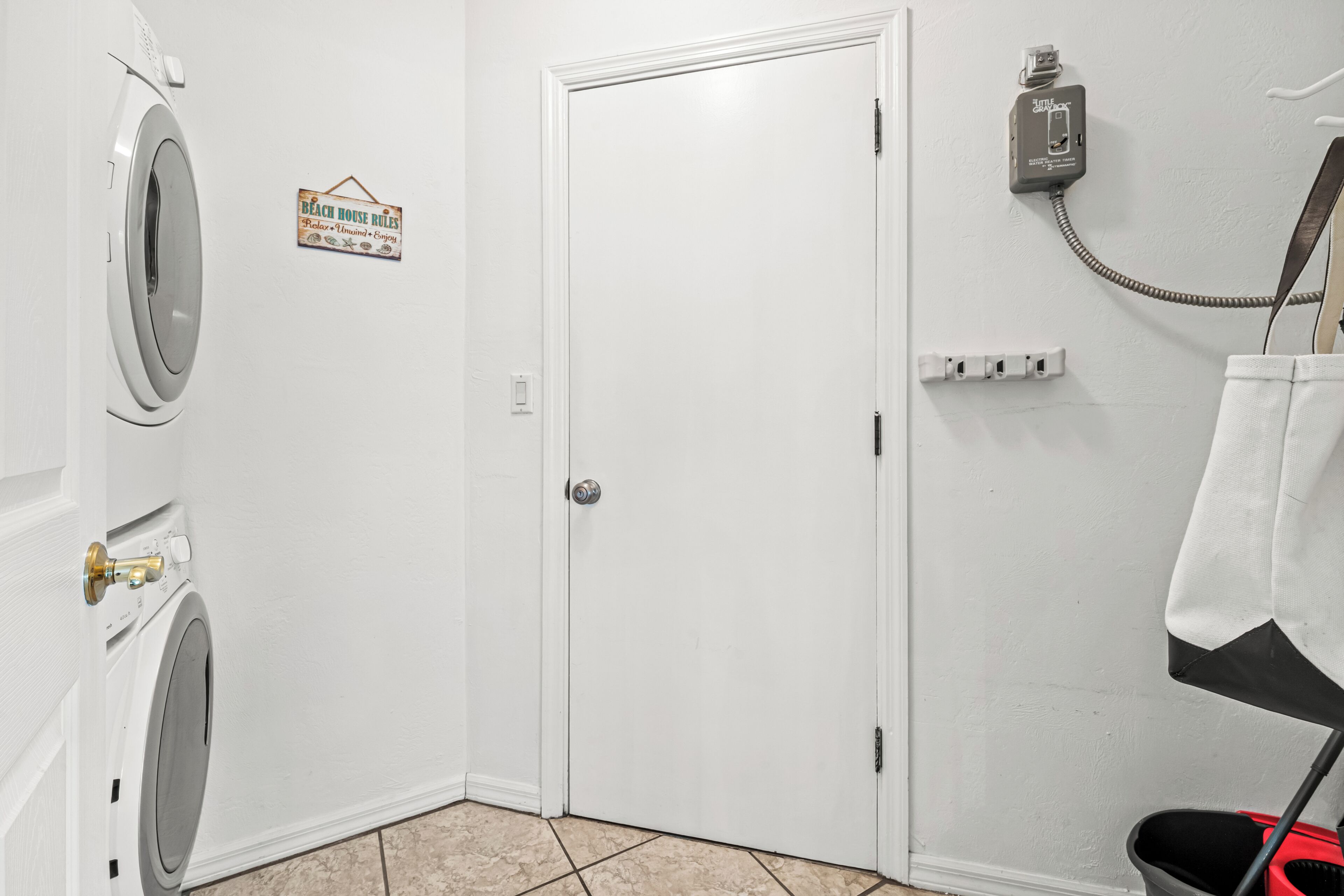 A laundry room with two washing machines, a door, a sign, a power outlet, and a hanging rack.