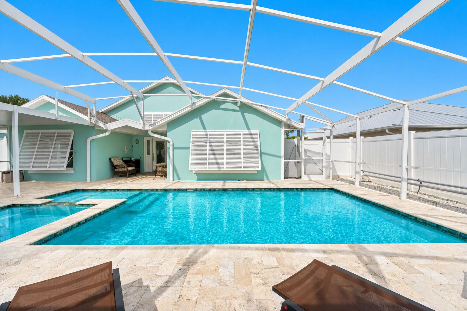 A swimming pool with a clear blue water, surrounded by a white fence, and a house with a light green exterior.