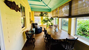 A dining area with a wooden table and chairs, a blue armchair, and a large window with blinds. - Historic 7-bedroom home in the heart of downtown in private setting,Pet friendly (New Shoreham)