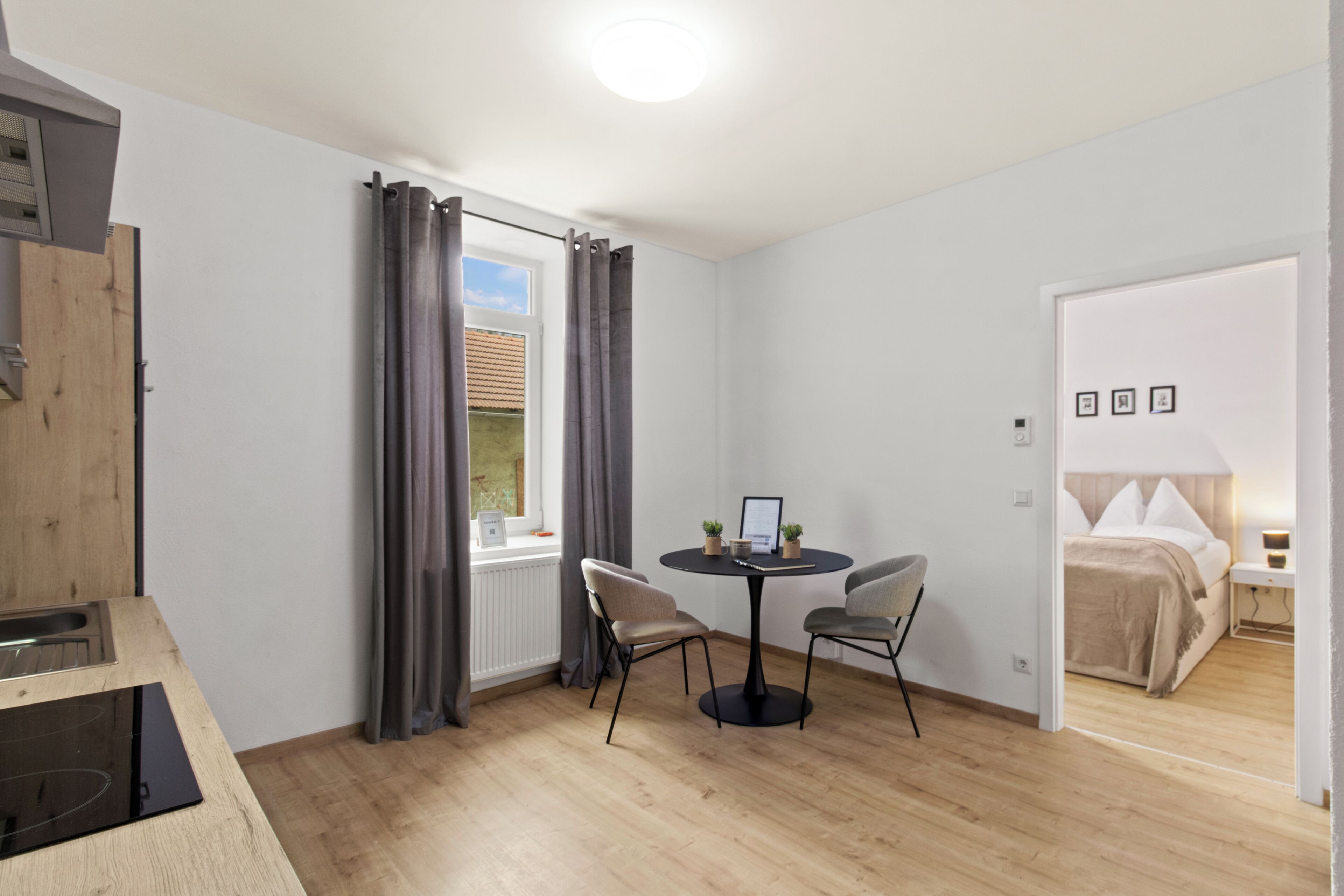 A modern room with a dining table, two chairs, a bed, and a window with curtains.