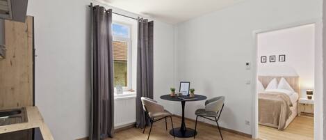 Una habitación moderna con una mesa de comedor, dos sillas, una cama y una ventana con cortinas.