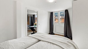 Ein Schlafzimmer mit Bett, einem Fenster mit Vorhängen, einem Heizkörper und Blick auf Gebäude.