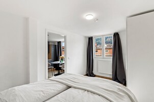 Ein Schlafzimmer mit Bett, einem Fenster mit Vorhängen, einem Heizkörper und Blick auf Gebäude.