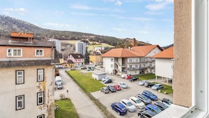 Ein Wohngebiet mit mehreren Mehrfamilienhäusern, einem Parkplatz mit verschiedenen Autos und einer hügeligen Landschaft im Hintergrund.