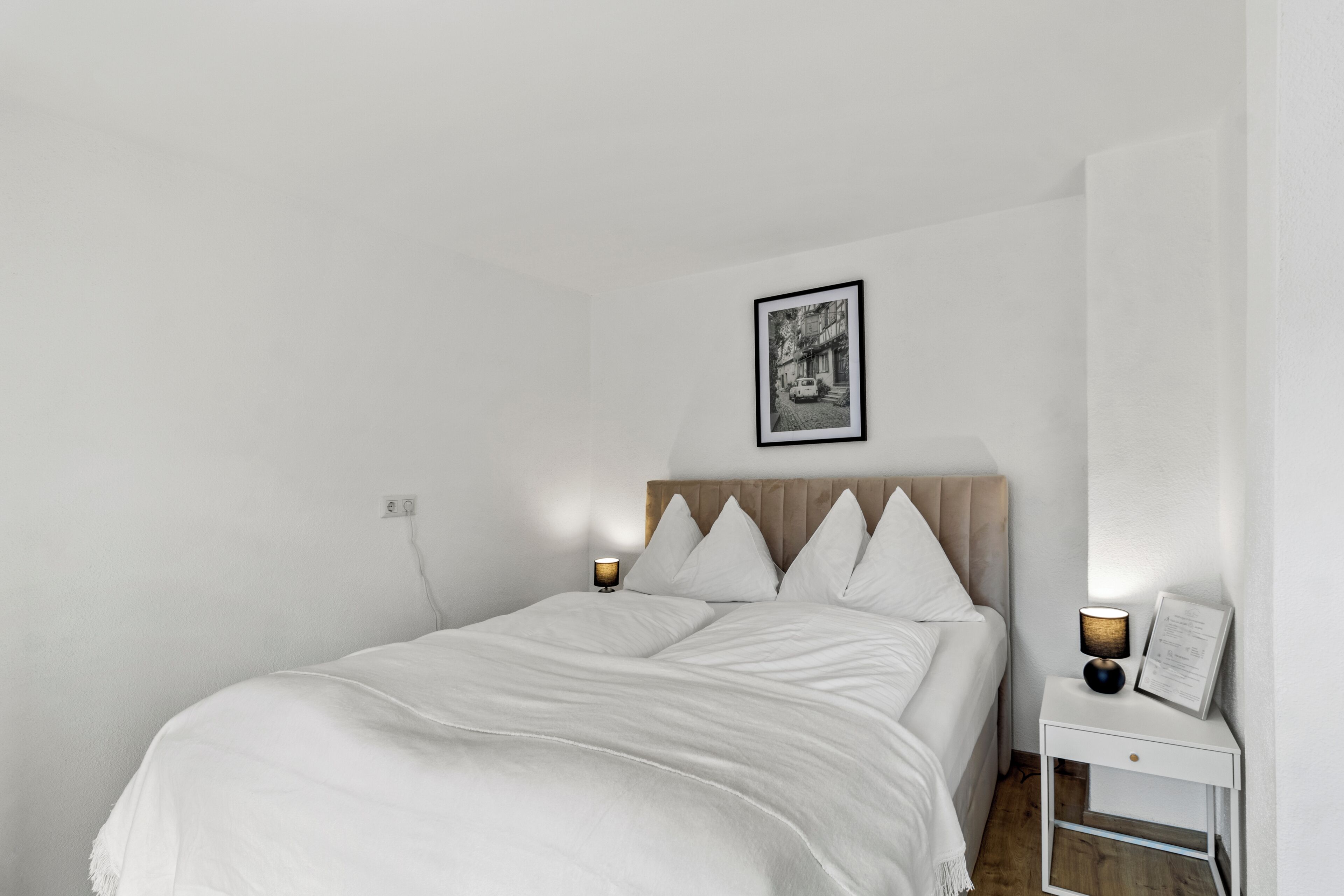 A minimalist bedroom with a bed, bedside lamps, a nightstand, and a framed picture on the wall.