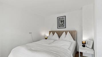 A minimalist bedroom with a bed, bedside lamps, a nightstand, and a framed picture on the wall.