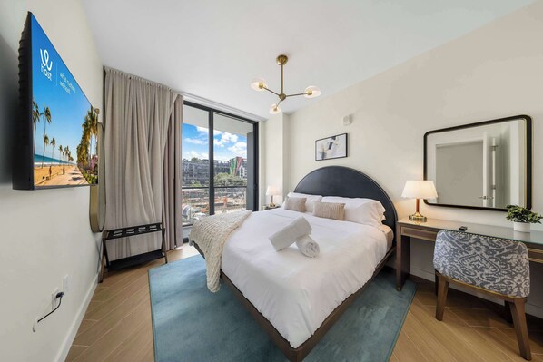 A hotel room with a bed, a desk, a chair, a large window, a ceiling light, and a poster on the wall. - 1BR + Balcony | Skyline Spa | Walk to Wynwood Walls (Miami)