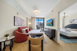 A modern hotel room with a bed, a sofa, a chair, a TV, and a balcony with a city view. - 1BR + Balcony | Skyline Spa | Walk to Wynwood Walls (Miami)
