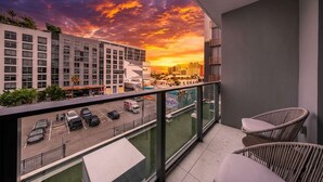 Ein Balkon mit Blick auf eine Stadtlandschaft bei Sonnenuntergang, ein Parkplatz und zwei Korbstühle.