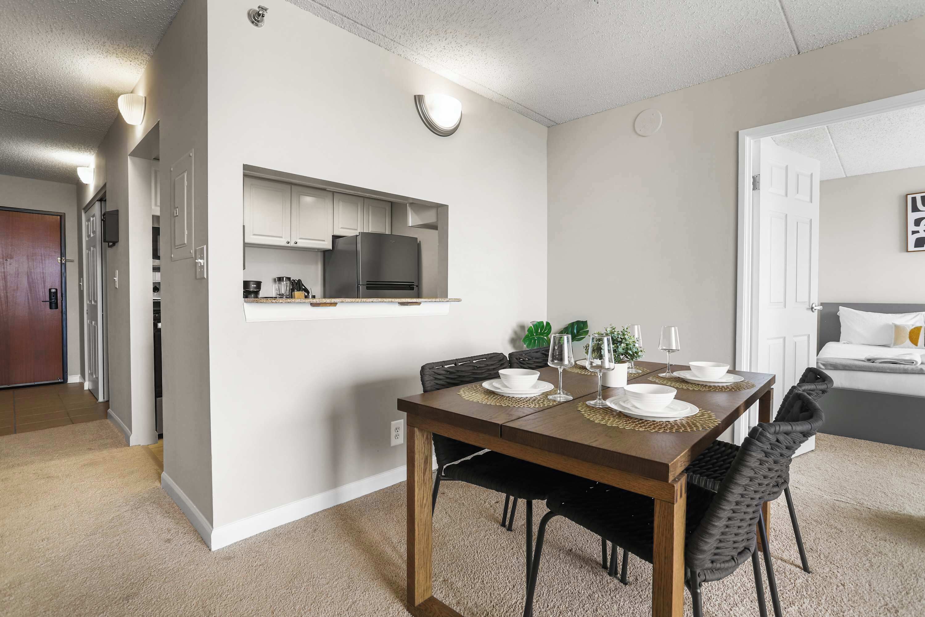 Un comedor con una mesa de madera, sillas negras y una cocina al fondo.
