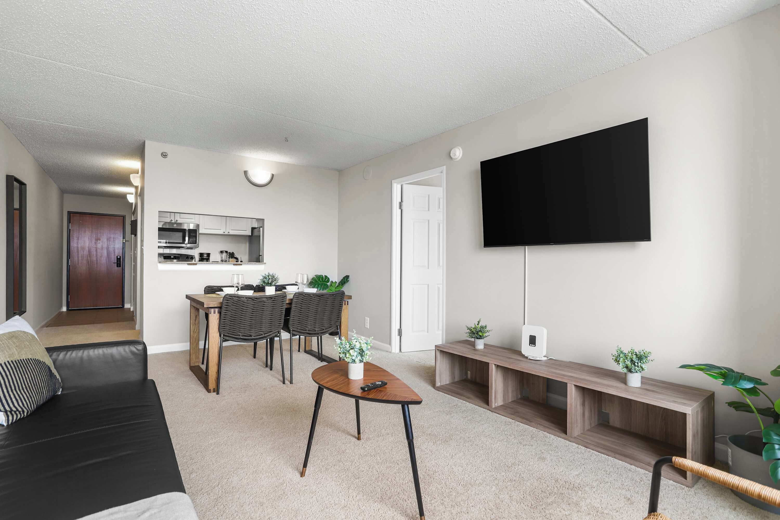 Een moderne woonkamer met een flatscreen-tv, een eethoek met een tafel en stoelen, en een keuken op de achtergrond.