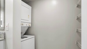 A laundry room with a white washer and dryer, a countertop, and a wall-mounted shelf unit.