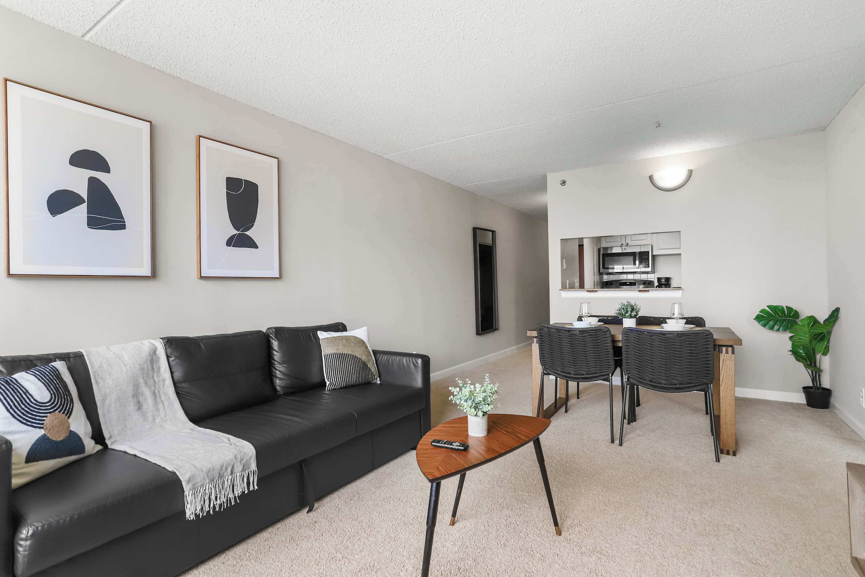 A modern living room with a black leather sofa, a coffee table, and a dining area with a wooden table and chairs.