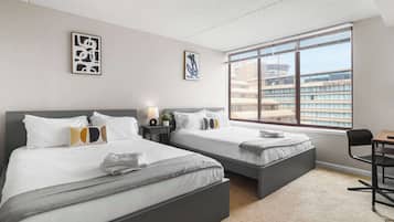 Habitación de hotel con dos camas, un escritorio y un amplio ventanal con vistas a edificios.