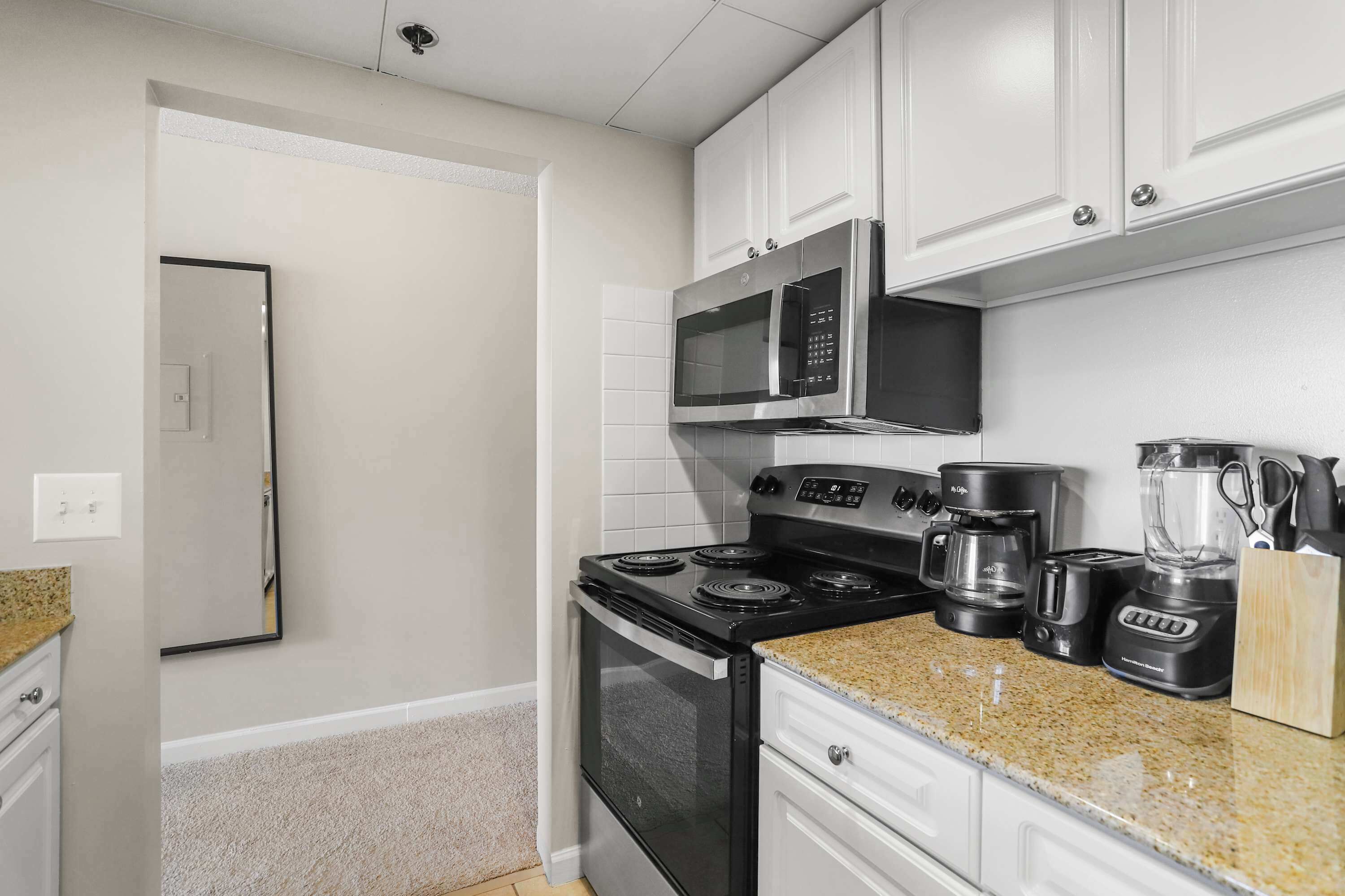 A kitchen with white cabinets, a stainless steel stove, a microwave, a coffee maker, and a blender.