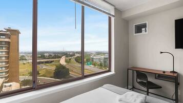Habitación de hotel con un ventanal grande que ofrece vistas a una autopista y edificios circundantes.