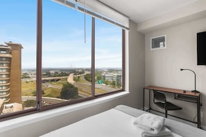 Habitación de hotel con un ventanal grande que ofrece vistas a una autopista y edificios circundantes.