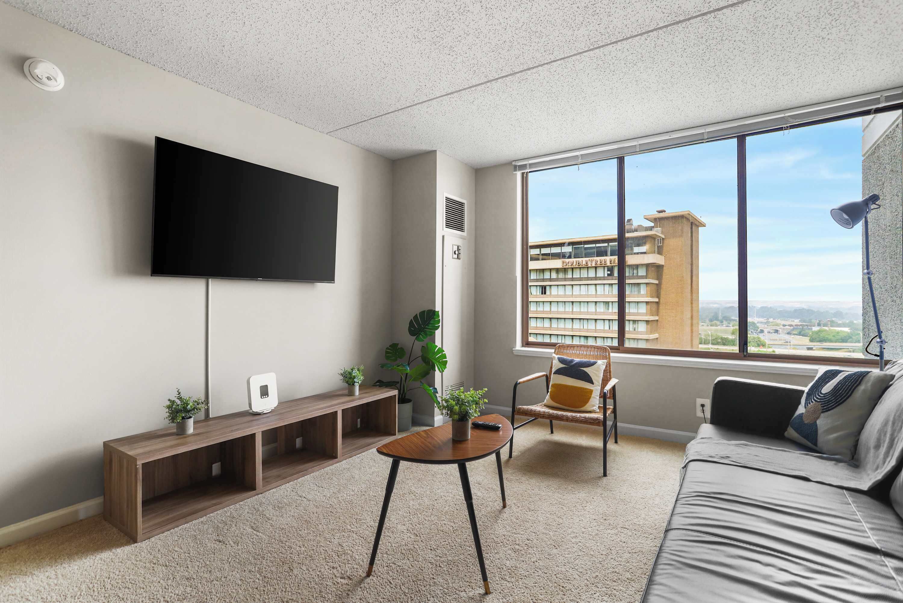 A modern living room with a flat-screen TV, a wooden console table, a round coffee table, a sofa, and a large window offering a city view.
