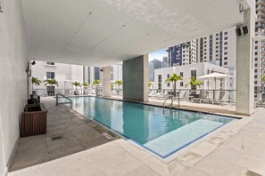 Ein Pool auf dem Dach mit Liegestühlen, einem kleinen Billardtisch und Blick auf hohe Gebäude.
