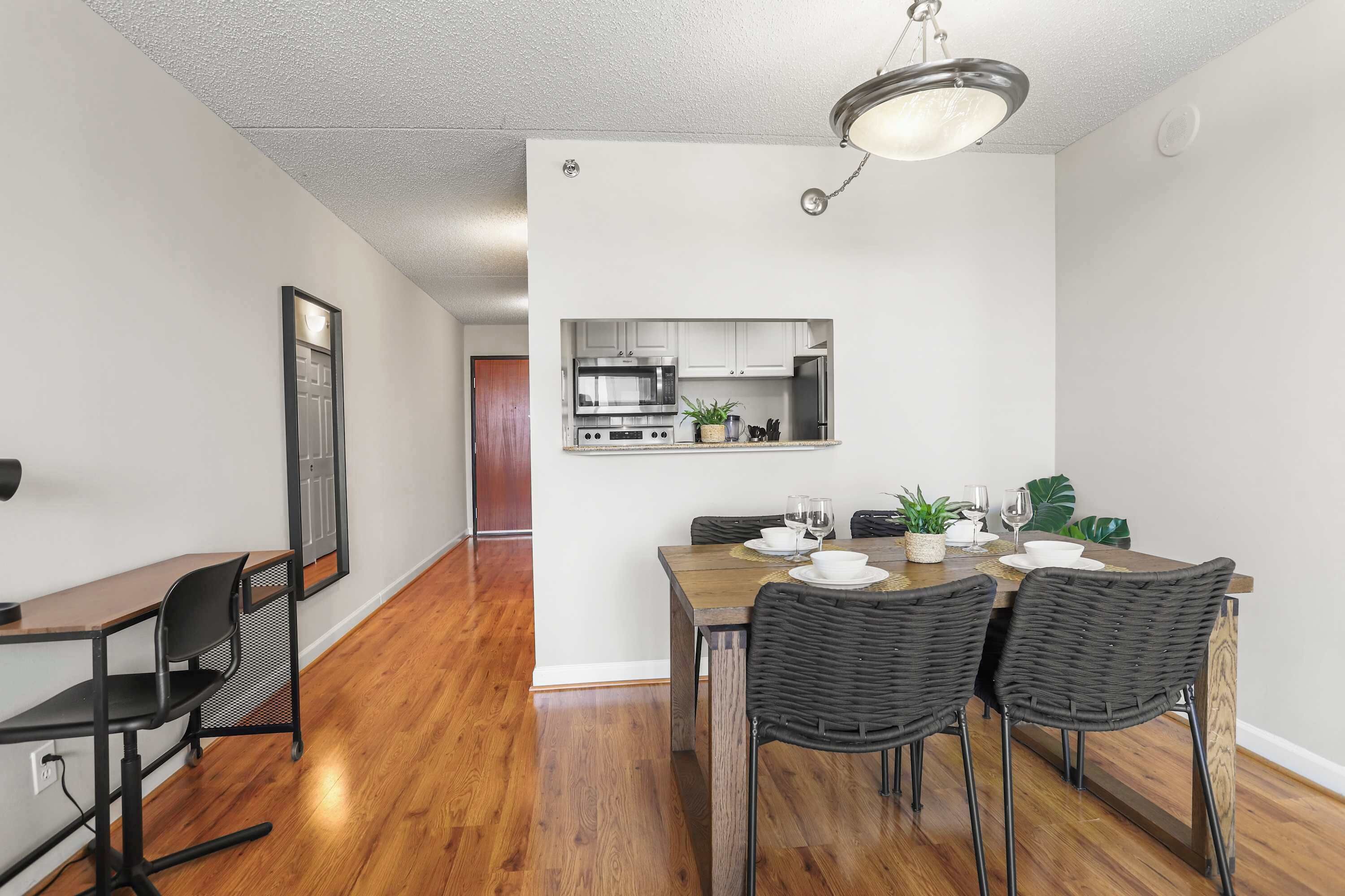A modern kitchen with stainless steel appliances, a dining area with a wooden table and wicker chairs, and a hallway with hardwood flooring.