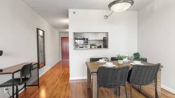 A modern kitchen with stainless steel appliances, a dining area with a wooden table and wicker chairs, and a hallway with hardwood flooring.