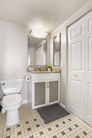 A bathroom with a toilet, sink, mirror, and a door. - Arlington Gem Stylish Apt | Near Fashion Centre (Arlington)