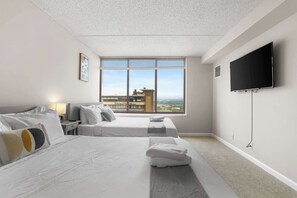 A hotel room with a large bed, two bedside tables, a flat-screen TV, and a window with a city view. - Arlington Gem Stylish Apt | Near Fashion Centre (Arlington)