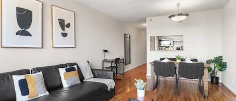Una sala de estar moderna con un sofá de cuero negro, una mesa de centro y un comedor con una mesa y sillas de madera.