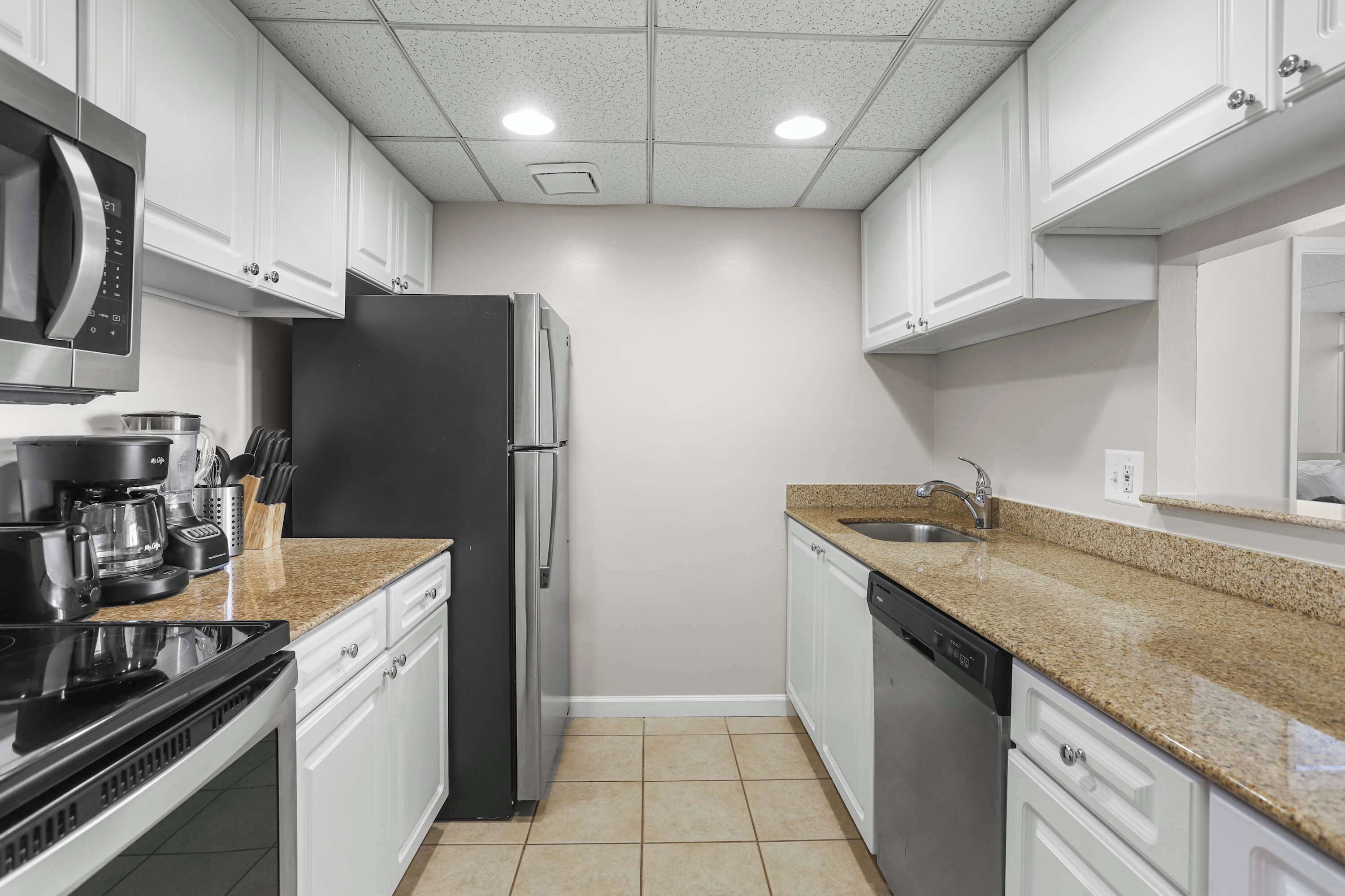 A modern kitchen with white cabinets, a stainless steel refrigerator, a coffee maker, and a dishwasher.