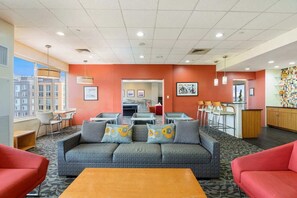 A hotel lobby with a grey sofa set, red armchairs, a coffee table, and a kitchen area with bar stools. - Arlington Gem Stylish Apt with Pool and Gym (Arlington)