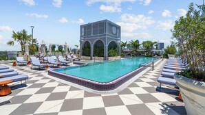 Ett poolområde på taket med solstolar, en swimmingpool och en modern byggnad med välvda fönster.