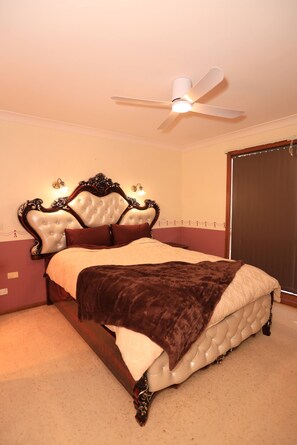 Un dormitorio con tablero de cama capitonado, ventilador de techo, cama con manta marrón y ventana con vistas.
