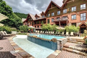 A hotel with a pool area, outdoor seating, and a mountainous backdrop. - Tremblant l Paradise | Ski in & Ski out | Spa&Pool (Mont-Tremblant)