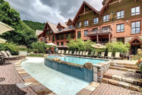A hotel with a pool area, outdoor seating, and a mountainous backdrop. - Tremblant l Paradise | Ski in & Ski out | Spa&Pool (Mont-Tremblant)