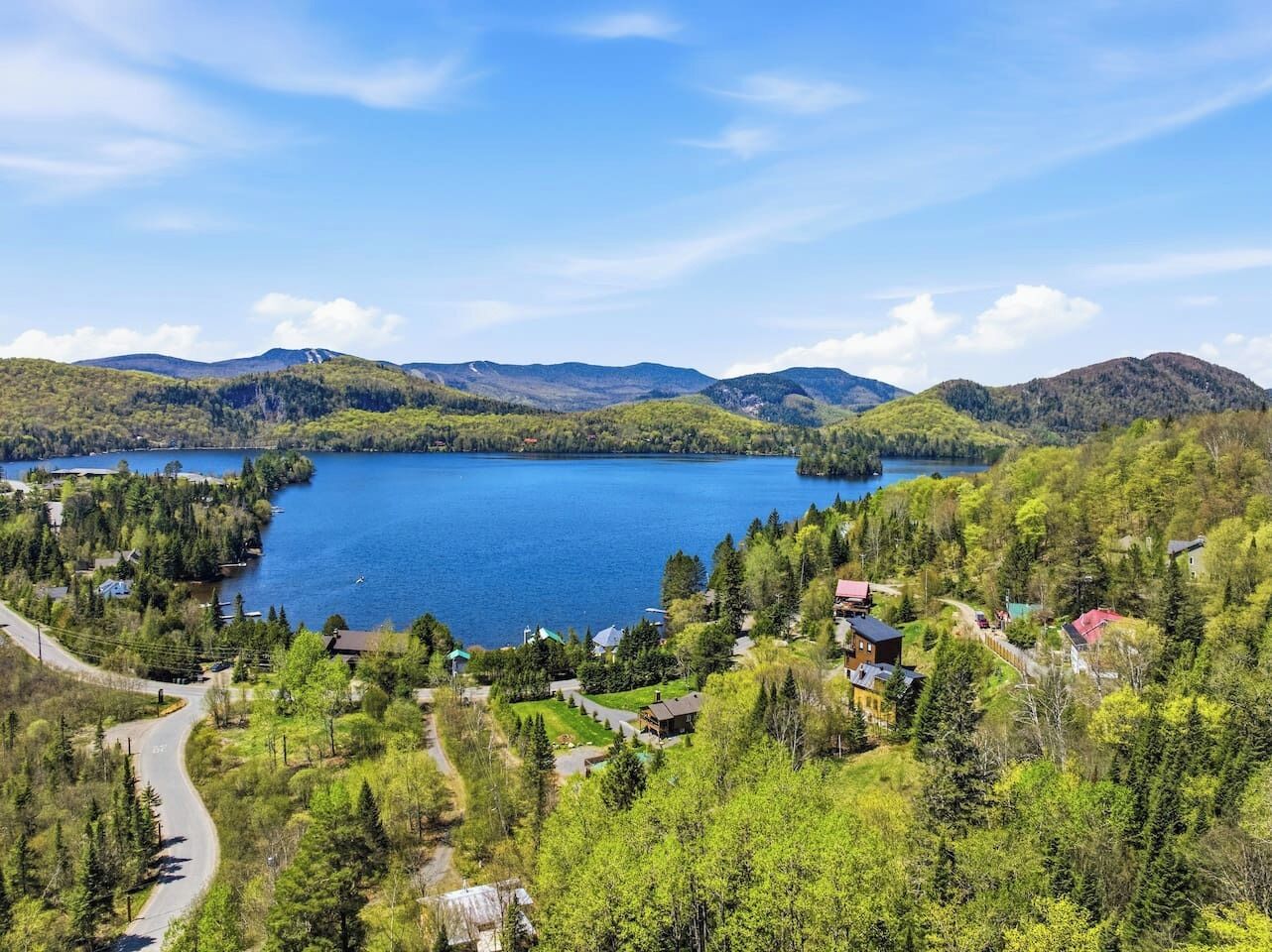 Una propiedad frente al lago con un camino que lleva a una cabaña, rodeada de bosque denso y montañas.
