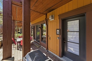 A covered outdoor seating area with a table and chairs, a wooden door with a number plate, and a vehicle parked outside. - Tremblant l Paradise | Ski in & Ski out | Spa&Pool (Mont-Tremblant)