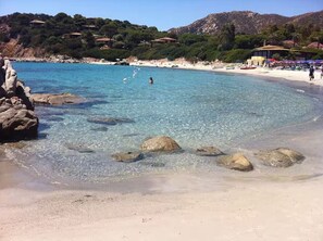 Una spiaggia con acqua cristallina, rocce e una persona che nuota.