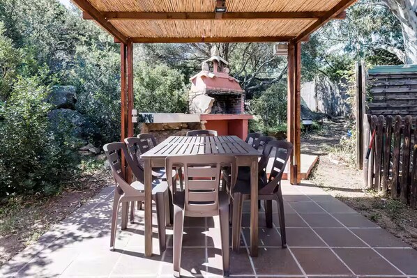 Un patio esterno con tavolo e sedie, un barbecue e una struttura a pergola.