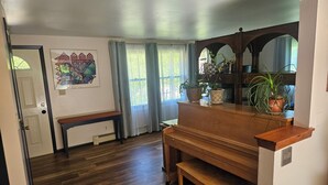 Una habitación con un piano de madera, un banco, una puerta y una ventana con cortinas.